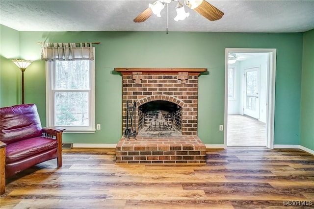 living area featuring a fireplace, a textured ceiling, baseboards, and wood finished floors