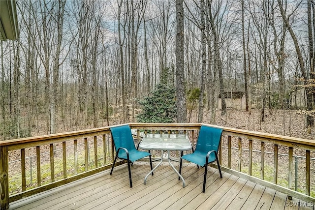 wooden deck with outdoor dining area and a wooded view