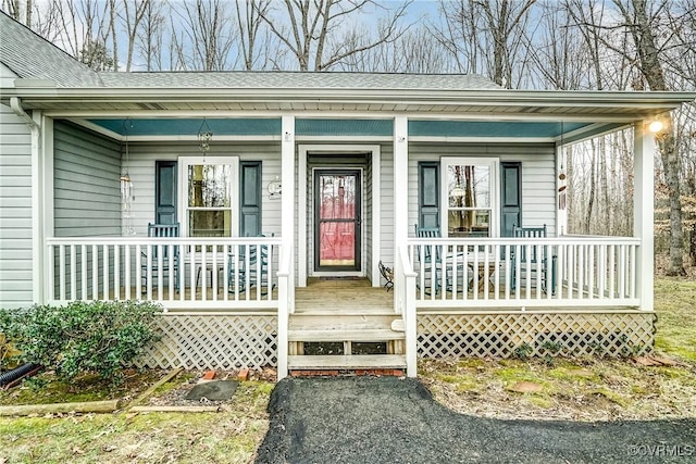 view of exterior entry featuring covered porch and roof with shingles