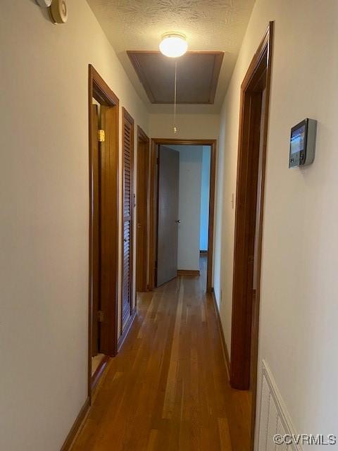 corridor featuring a textured ceiling, wood finished floors, attic access, and baseboards