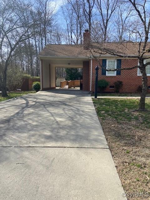 ranch-style home with a carport, concrete driveway, brick siding, and a chimney