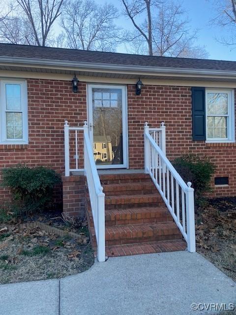 entrance to property featuring crawl space, roof with shingles, and brick siding