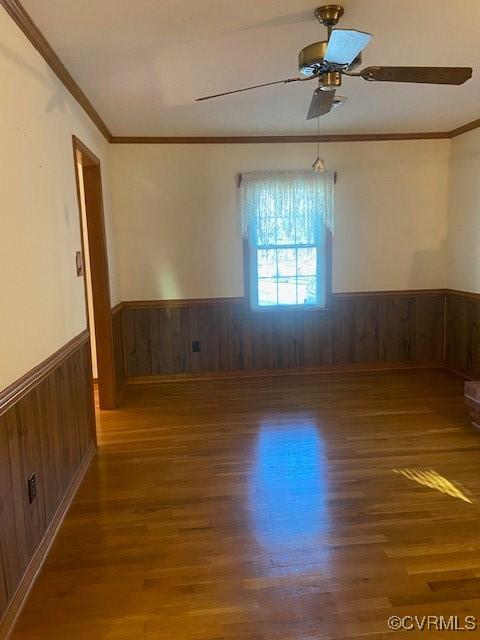 spare room with a wainscoted wall, crown molding, wood finished floors, and wooden walls