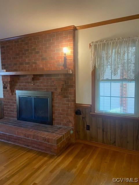 unfurnished living room with a wainscoted wall, wood walls, a brick fireplace, and wood finished floors