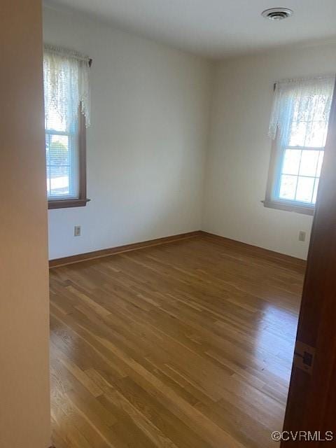 unfurnished room featuring baseboards, visible vents, and wood finished floors