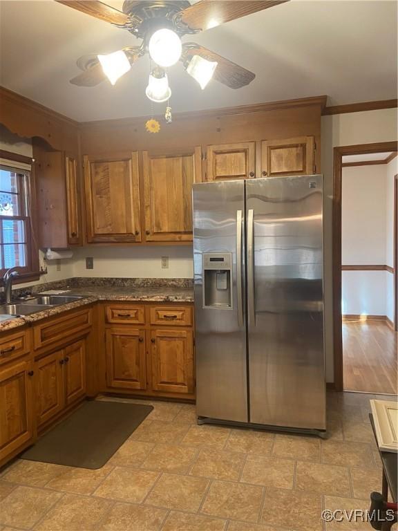 kitchen with brown cabinetry, stainless steel fridge with ice dispenser, ceiling fan, stone finish floor, and a sink