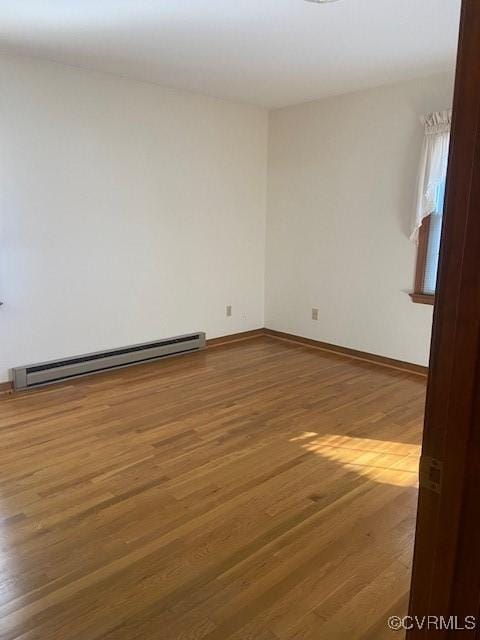 unfurnished room featuring a baseboard radiator, baseboards, and wood finished floors