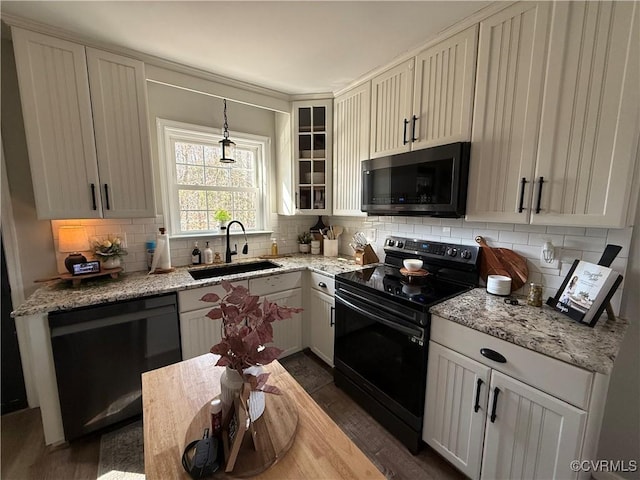 kitchen featuring light stone counters, a sink, black appliances, glass insert cabinets, and backsplash