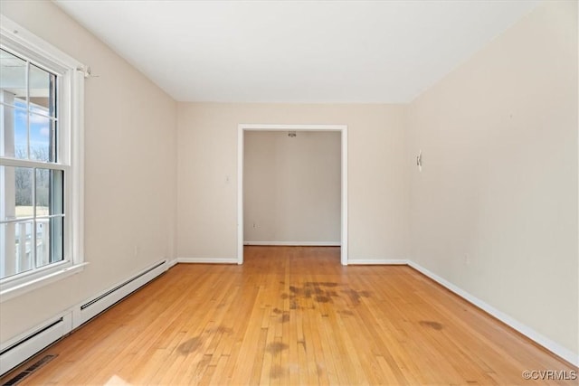 spare room featuring a baseboard heating unit, light wood finished floors, and baseboards