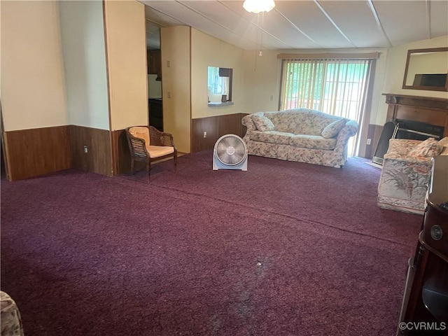carpeted living area featuring wainscoting, vaulted ceiling, wooden walls, and a fireplace