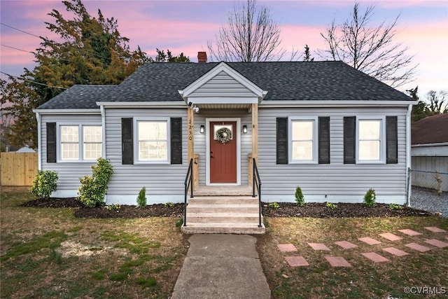 bungalow-style house featuring a shingled roof, a chimney, and fence