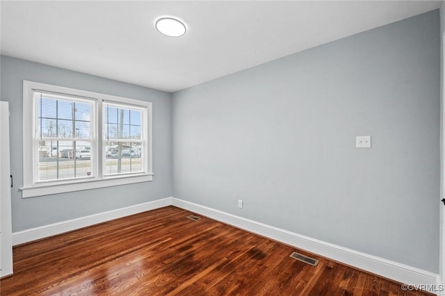 empty room featuring wood finished floors, visible vents, and baseboards