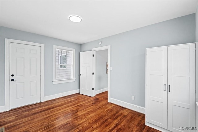 unfurnished bedroom with a closet, dark wood finished floors, and baseboards