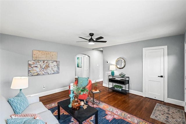 living room featuring a ceiling fan, arched walkways, baseboards, and wood finished floors