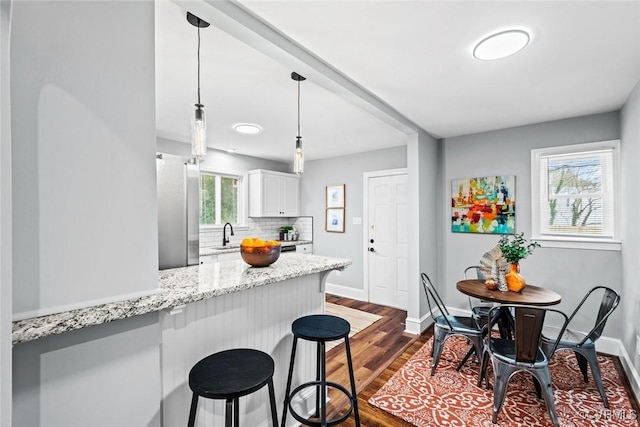 kitchen with white cabinets, decorative backsplash, dark wood-type flooring, freestanding refrigerator, and a kitchen bar