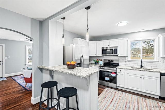 kitchen with stainless steel appliances, a sink, dark wood finished floors, tasteful backsplash, and a kitchen bar