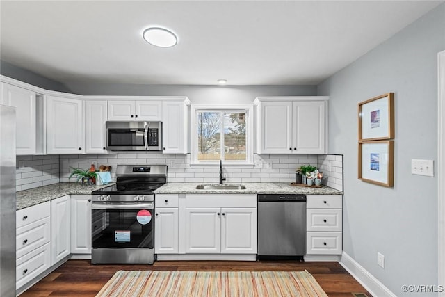 kitchen with stainless steel appliances, a sink, light stone counters, and dark wood-style floors