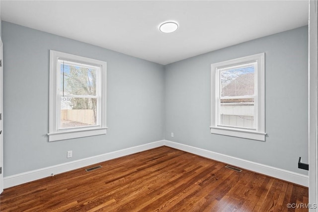 unfurnished room with dark wood-type flooring, visible vents, and baseboards