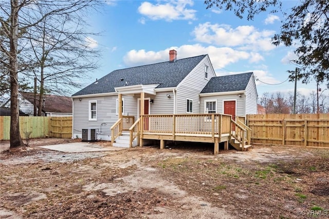 back of property featuring a deck, central AC unit, a fenced backyard, roof with shingles, and a chimney