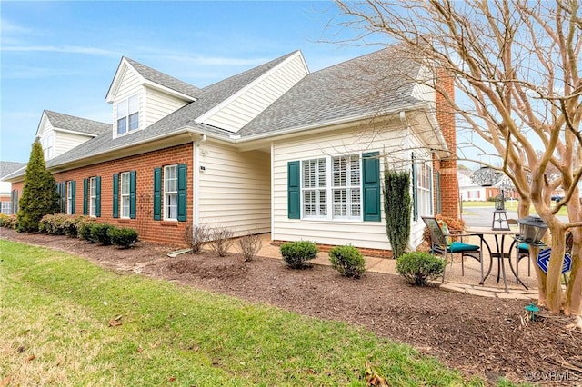 view of property exterior with a patio area, roof with shingles, a lawn, and brick siding