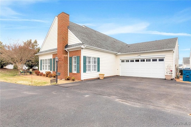 view of front of house with driveway, a shingled roof, a chimney, an attached garage, and brick siding