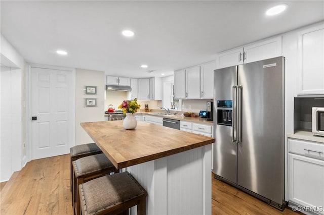 kitchen featuring stainless steel appliances, wooden counters, a sink, light wood-type flooring, and under cabinet range hood