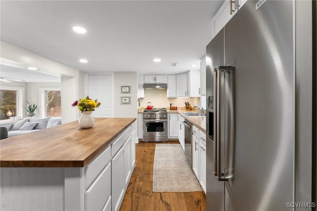 kitchen featuring dark wood-style flooring, high end appliances, butcher block counters, a sink, and under cabinet range hood