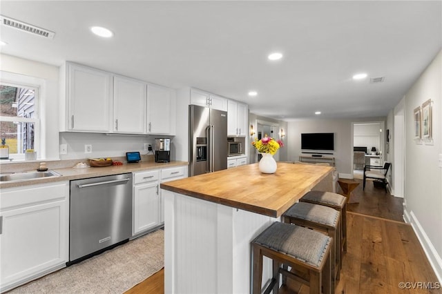 kitchen featuring white cabinets, stainless steel appliances, visible vents, and a kitchen breakfast bar