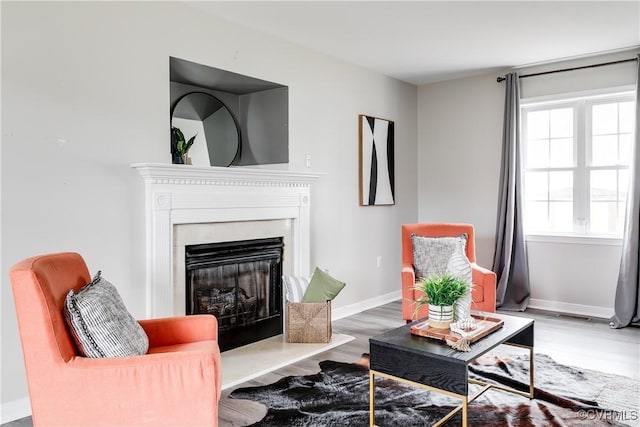 living area with visible vents, a fireplace with raised hearth, baseboards, and wood finished floors