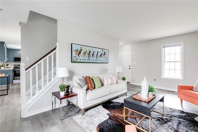 living room featuring stairway, baseboards, visible vents, and light wood finished floors