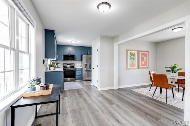 interior space featuring light wood finished floors, blue cabinetry, baseboards, light countertops, and appliances with stainless steel finishes