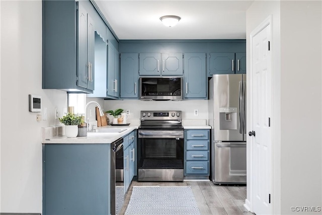 kitchen featuring a sink, blue cabinetry, stainless steel appliances, light wood-style floors, and light countertops