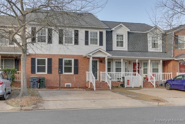 view of property featuring a shingled roof, brick siding, and a porch