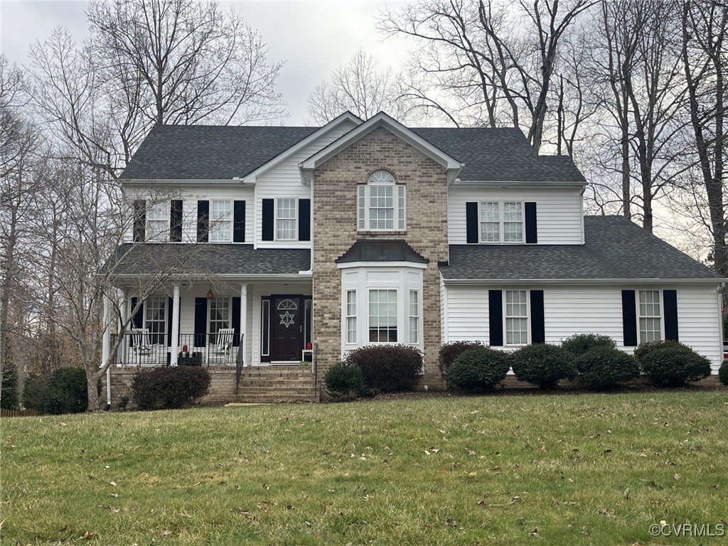 colonial inspired home featuring a porch, brick siding, a front yard, and a shingled roof