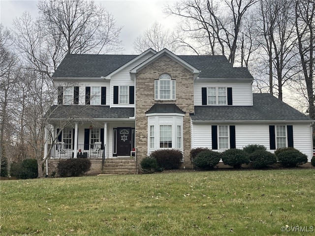 colonial inspired home featuring a porch, brick siding, a front yard, and a shingled roof