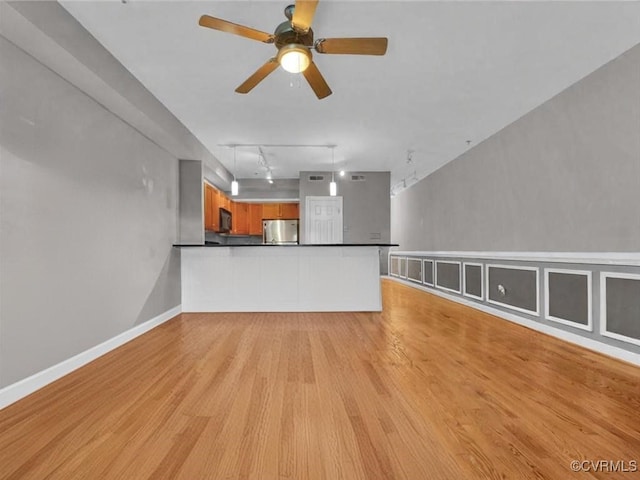 unfurnished living room featuring a ceiling fan, rail lighting, light wood-style flooring, and baseboards