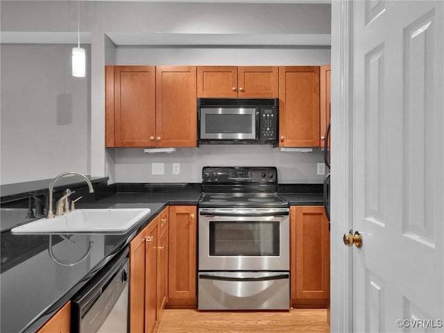 kitchen featuring a sink, appliances with stainless steel finishes, light wood finished floors, brown cabinetry, and dark countertops