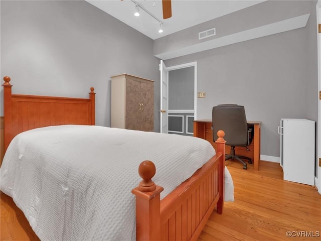 bedroom featuring light wood finished floors, rail lighting, visible vents, a ceiling fan, and baseboards