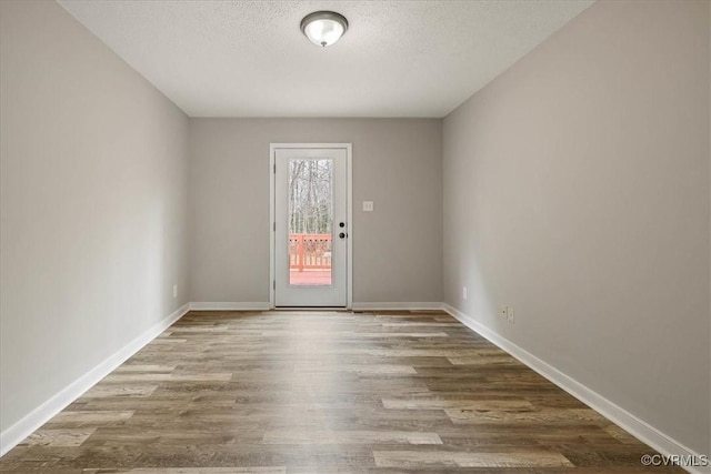 unfurnished room with wood finished floors, baseboards, and a textured ceiling