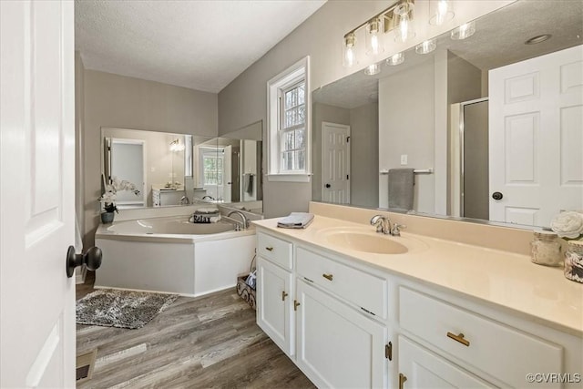 bathroom featuring vanity, wood finished floors, a stall shower, a textured ceiling, and a garden tub