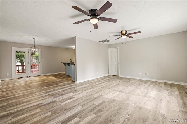 unfurnished living room featuring visible vents, a textured ceiling, light wood-style flooring, and ceiling fan with notable chandelier