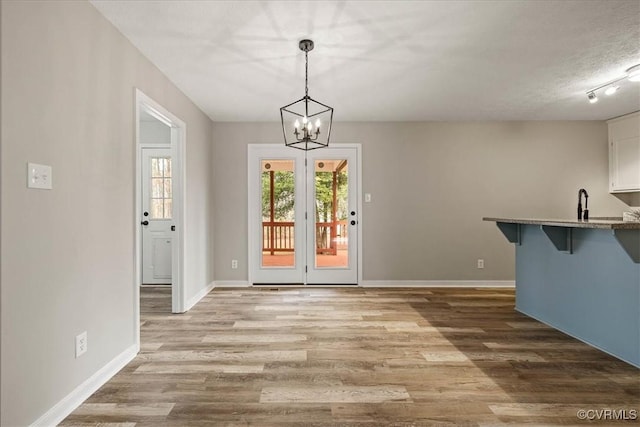 unfurnished dining area featuring wood finished floors, baseboards, a sink, a textured ceiling, and a chandelier