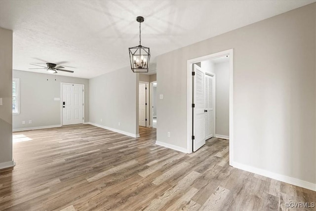 spare room with light wood-style flooring, ceiling fan with notable chandelier, and baseboards