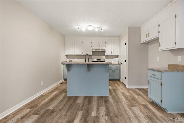 kitchen with under cabinet range hood, stainless steel range oven, white cabinets, and light wood-style flooring