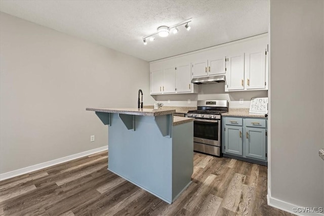 kitchen featuring under cabinet range hood, a breakfast bar, stainless steel gas range, white cabinets, and a textured ceiling