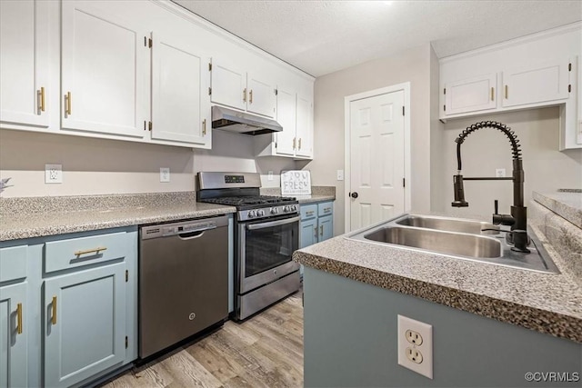 kitchen featuring light wood-type flooring, under cabinet range hood, a sink, white cabinetry, and appliances with stainless steel finishes