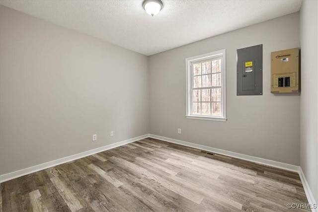 spare room with electric panel, a textured ceiling, baseboards, and wood finished floors