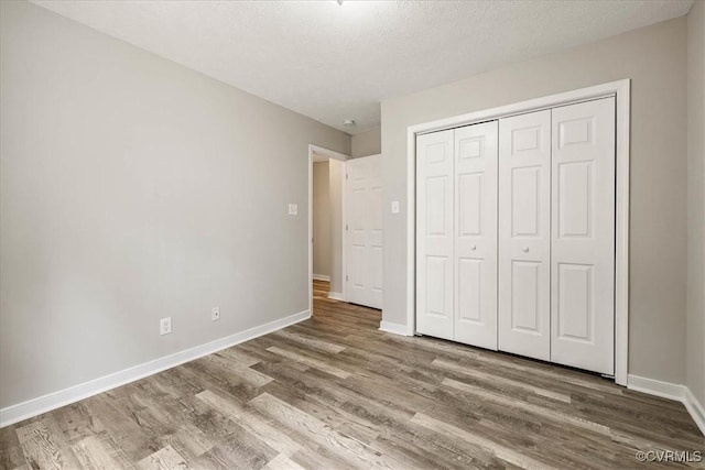 unfurnished bedroom with a closet, baseboards, a textured ceiling, and wood finished floors