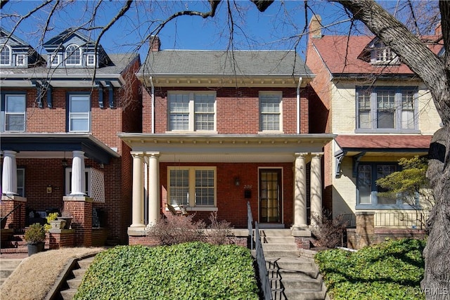 view of front of home featuring covered porch, brick siding, and a chimney