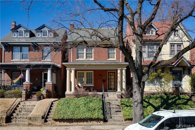 view of front of property with stairs, brick siding, covered porch, and a chimney